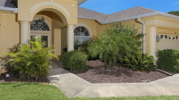A residential house with a yellow facade, arched windows, and a well-maintained garden with various plants. - Parrot's Paradise - spacious walk to beach pool home with privacy (Englewood)