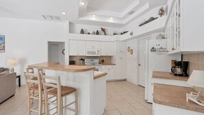 A modern kitchen with white cabinets, a wooden island, and a coffee machine. - Parrot's Paradise - spacious walk to beach pool home with privacy (Englewood)