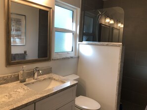 Features a granite countertop sink, white toilet, and glass-enclosed shower area.