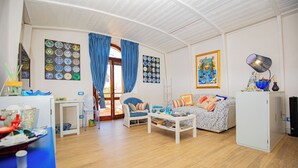 A living room with a sofa, coffee table, and a white cabinet. There are curtains, a framed artwork, and a lamp on a side table. - 50 steps from the Mare Superior (Orbetello)