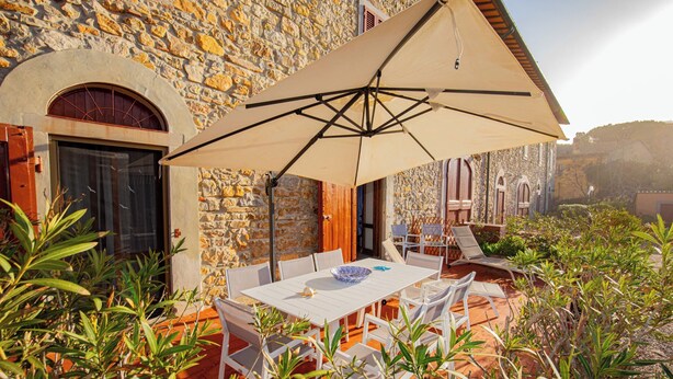 A stone building with a tiled patio, white furniture, and a large umbrella. - 50 steps from the Mare Superior (Orbetello)