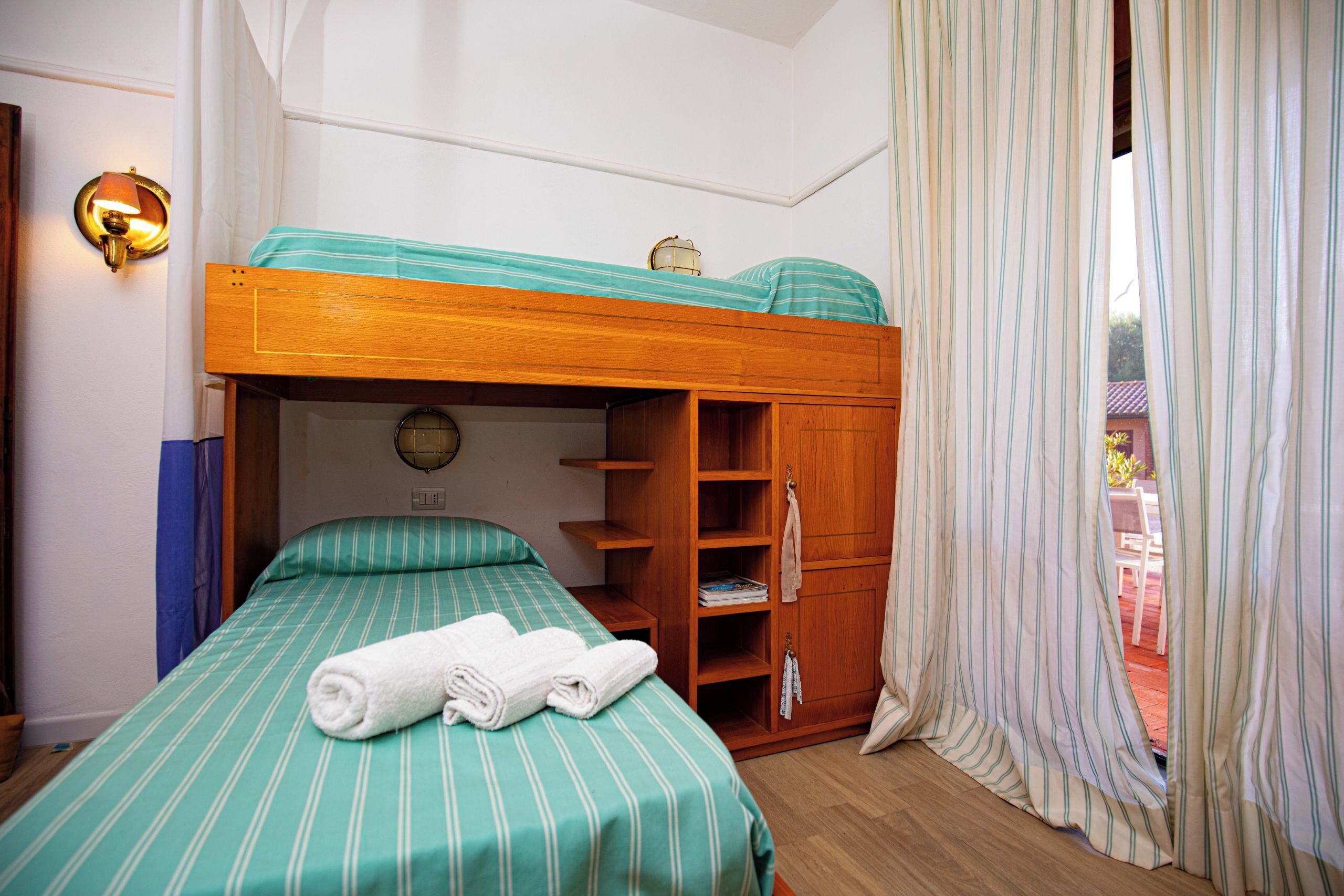 A bunk bed with a green-striped bedspread, a wooden wardrobe, and a wall-mounted lamp.