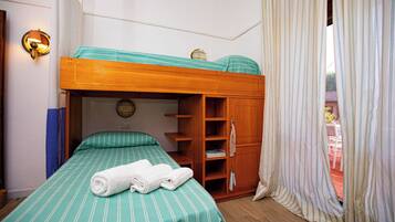 A bunk bed with a green-striped bedspread, a wooden wardrobe, and a wall-mounted lamp.