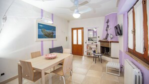 A dining area with a wooden table and chairs, a ceiling fan, and a bookshelf with books and decorative items. - Seaside apartment in Bengodi (Fonteblanda)