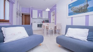 A modern living room with two sofas, a dining table, and a kitchen area. - Seaside apartment in Bengodi (Fonteblanda)