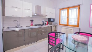 A modern kitchen with stainless steel appliances, a glass dining table, and a window with wooden frames. - Seaside apartment in Bengodi (Orbetello)
