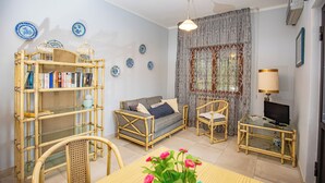 A living room with a sofa, chairs, a table with flowers, a TV, and a bookshelf. - Seaside apartment in Bengodi (Fonteblanda)