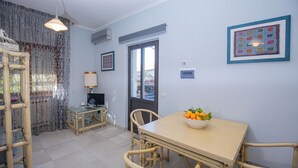A dining area with a table, chairs, a television, and a window with curtains. - Seaside apartment in Bengodi (Fonteblanda)