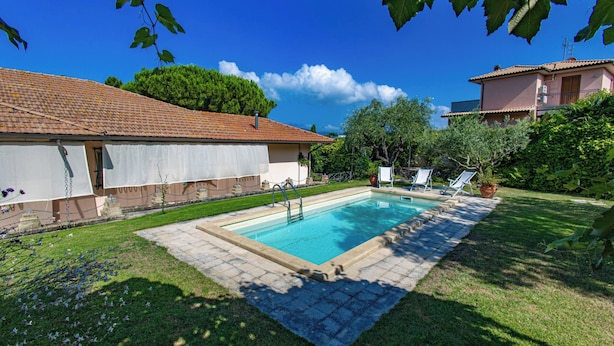 A swimming pool with a tiled deck, surrounded by a grassy lawn and a house with a tiled roof. - Seaside apartment in Bengodi (Fonteblanda)