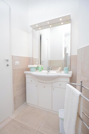 Ein modernes Badezimmer mit einem weißen Waschbecken, einem Spiegel und einem gefliesten Boden.