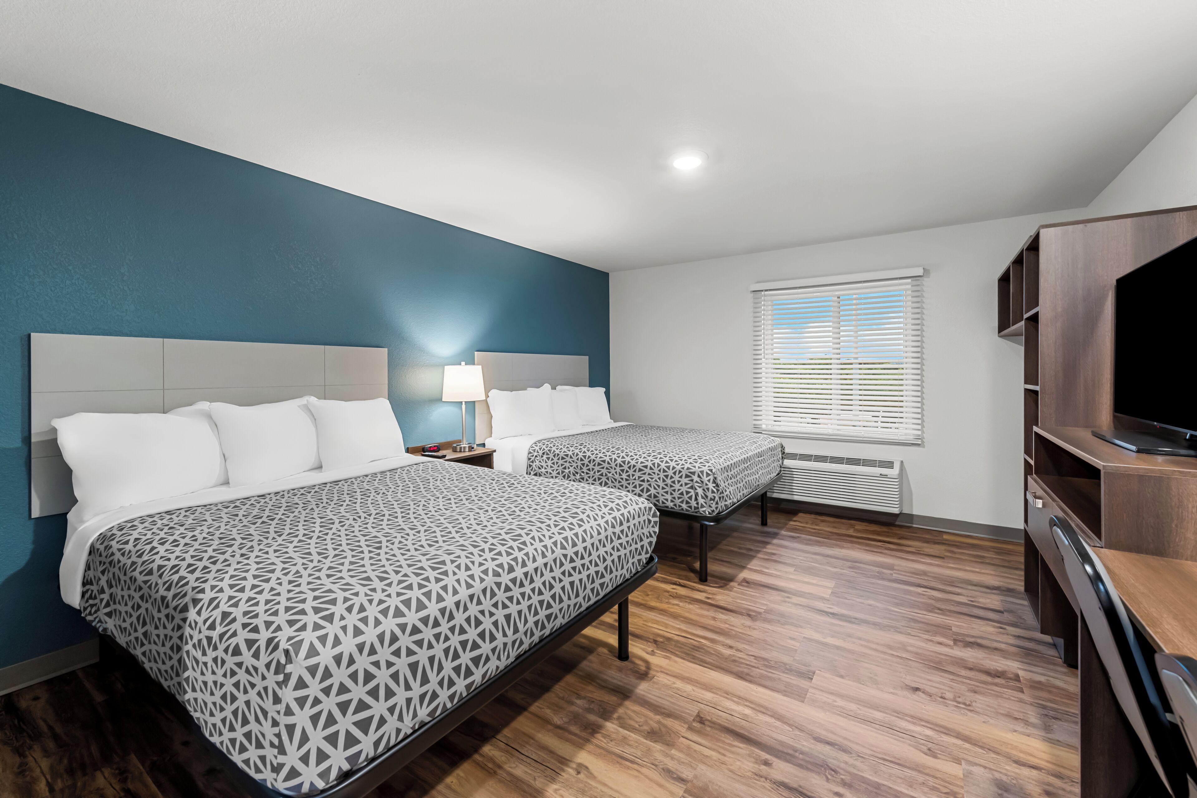 A hotel room with two beds, a TV, and a desk.