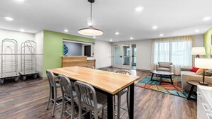 A modern hotel room with a wooden dining table, metal chairs, a sofa, a small round table, and a lamp. - Woodspring Suites Kansas City Airport (Kansas City)