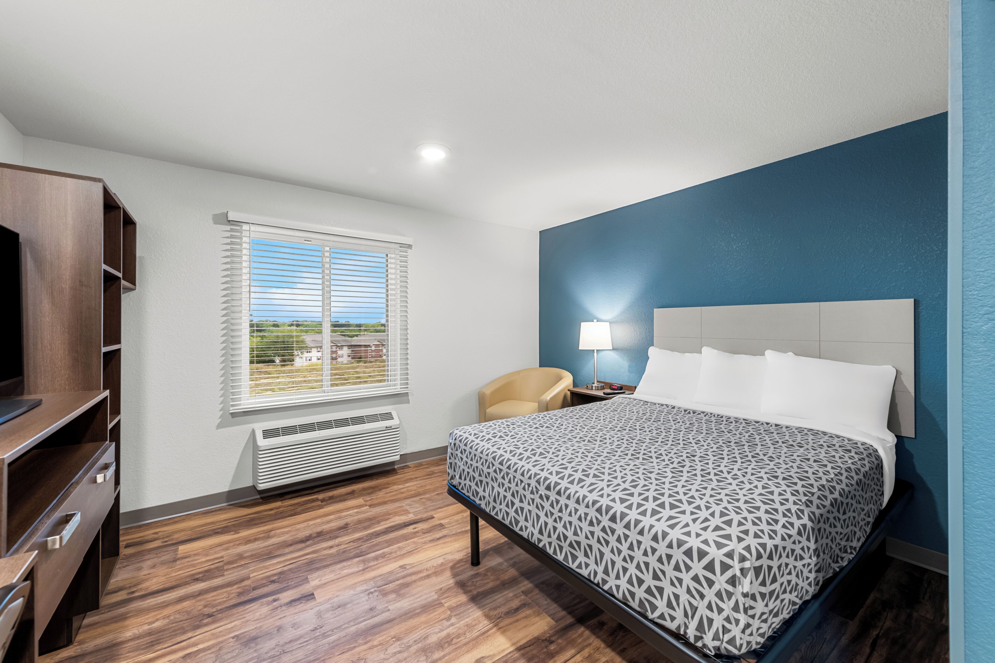 A bedroom with a bed, a chair, a desk, and a window with blinds.