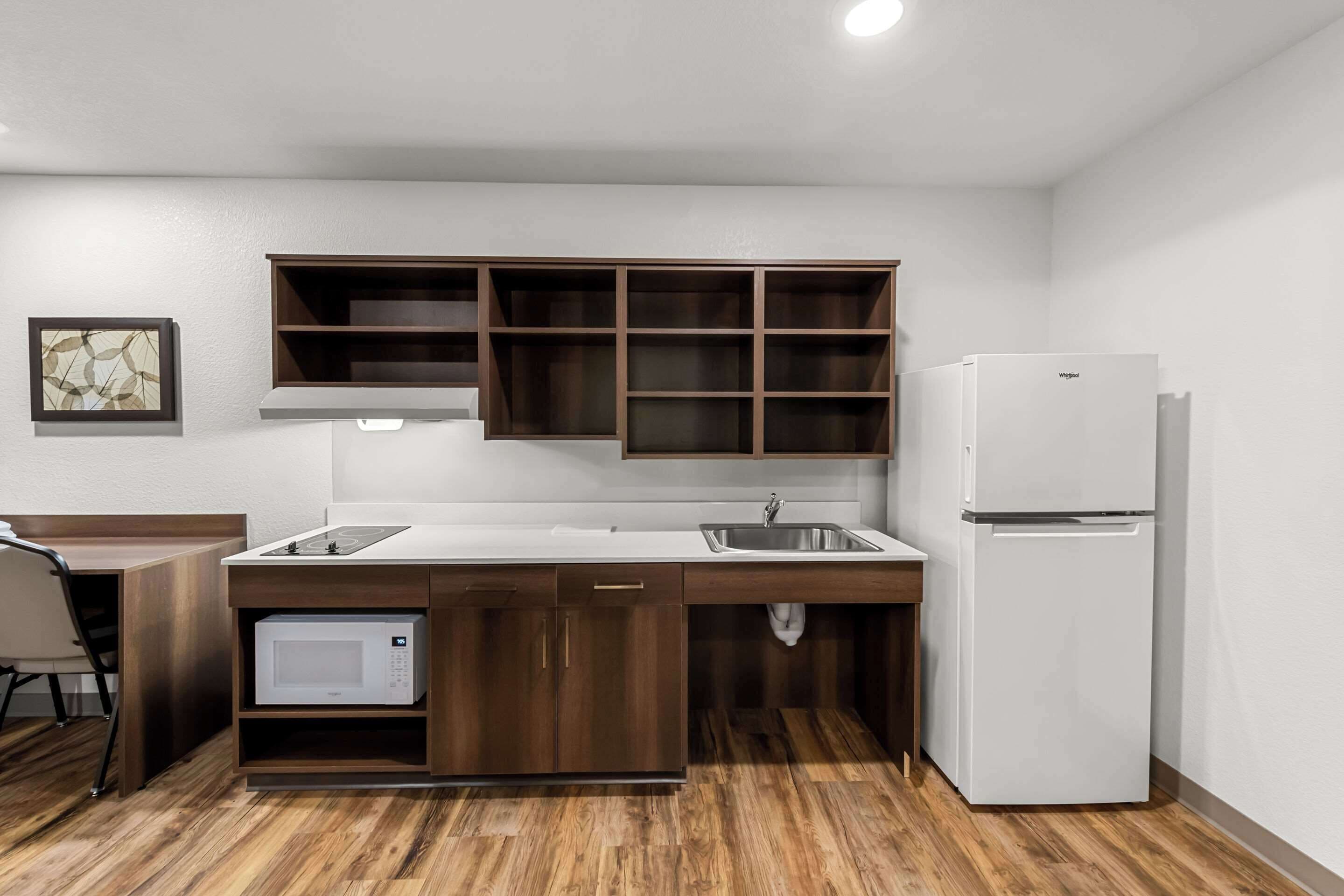 A compact kitchen with wooden cabinets, a white countertop, a built-in microwave, and a white refrigerator.