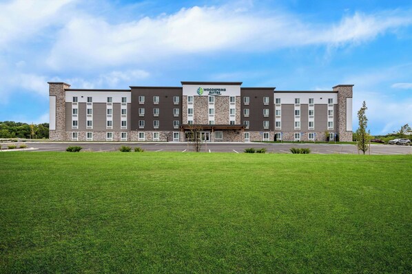 A multi-story hotel with a central entrance, surrounded by a well-maintained lawn and parking area. - Woodspring Suites Kansas City Airport (Kansas City)