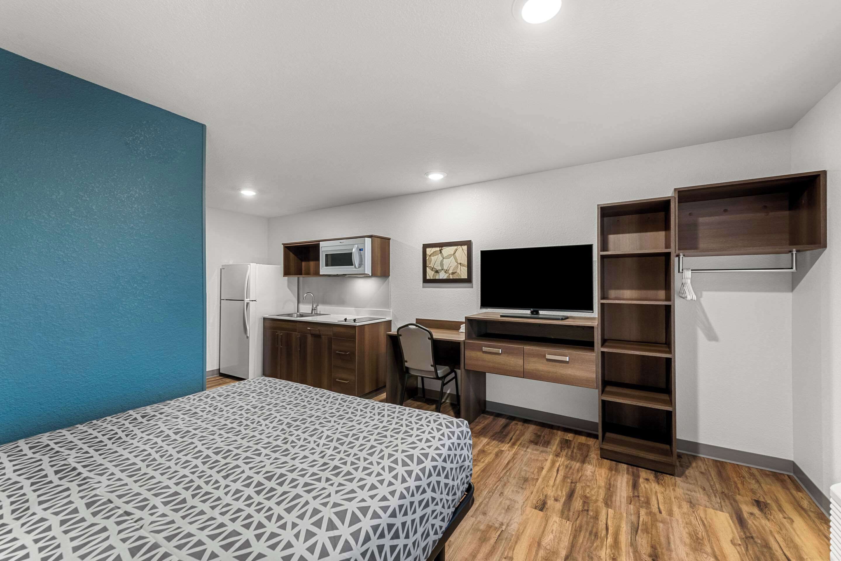 A compact room with a bed, kitchenette, desk, and a TV.