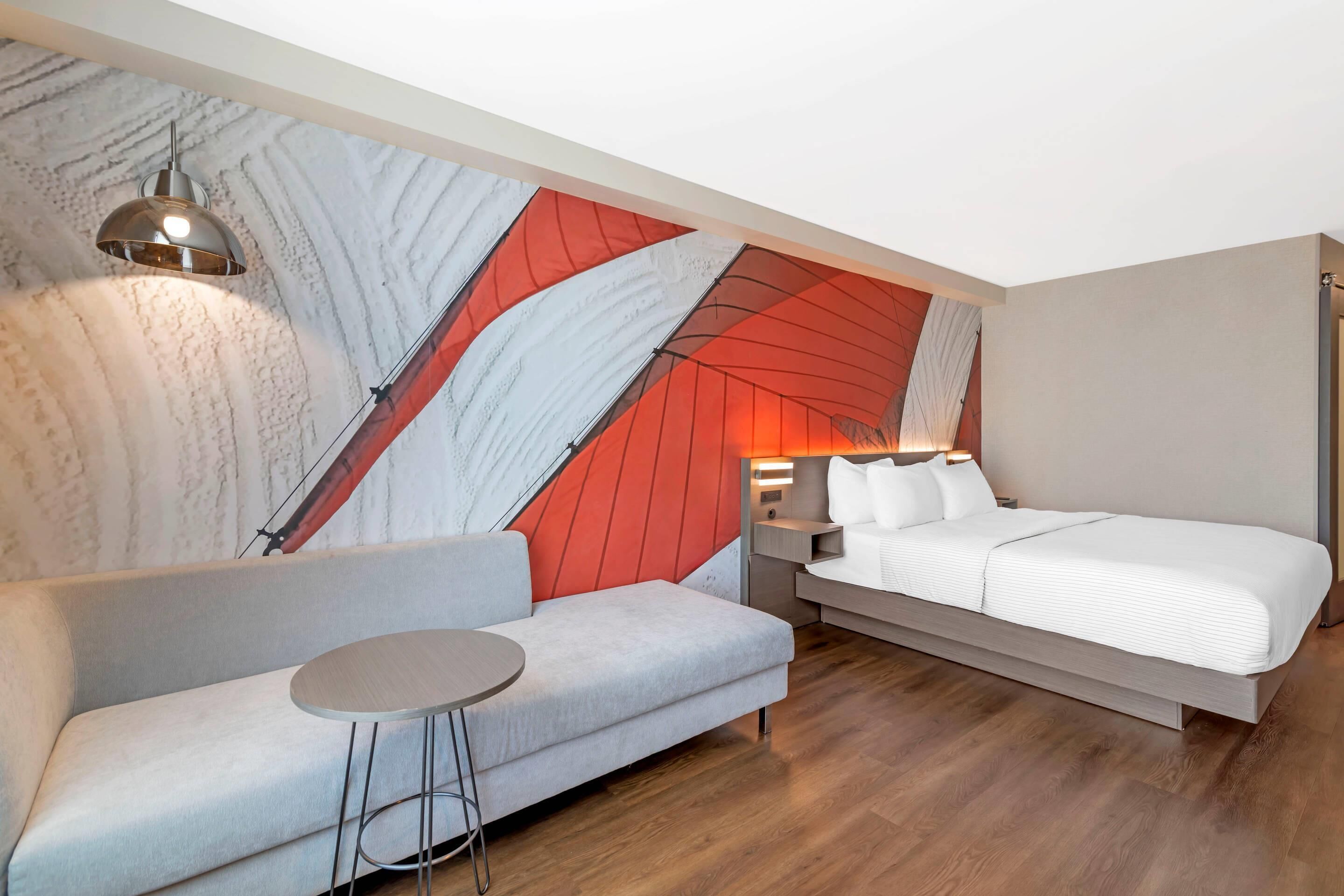 Ein modernes Hotelzimmer mit einer Couch, einem Bett, einem runden Tisch und einer einzigartigen Wandmalerei.