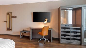 A hotel room with a bed, a desk with a chair, a television, a wardrobe, and a bedside table.