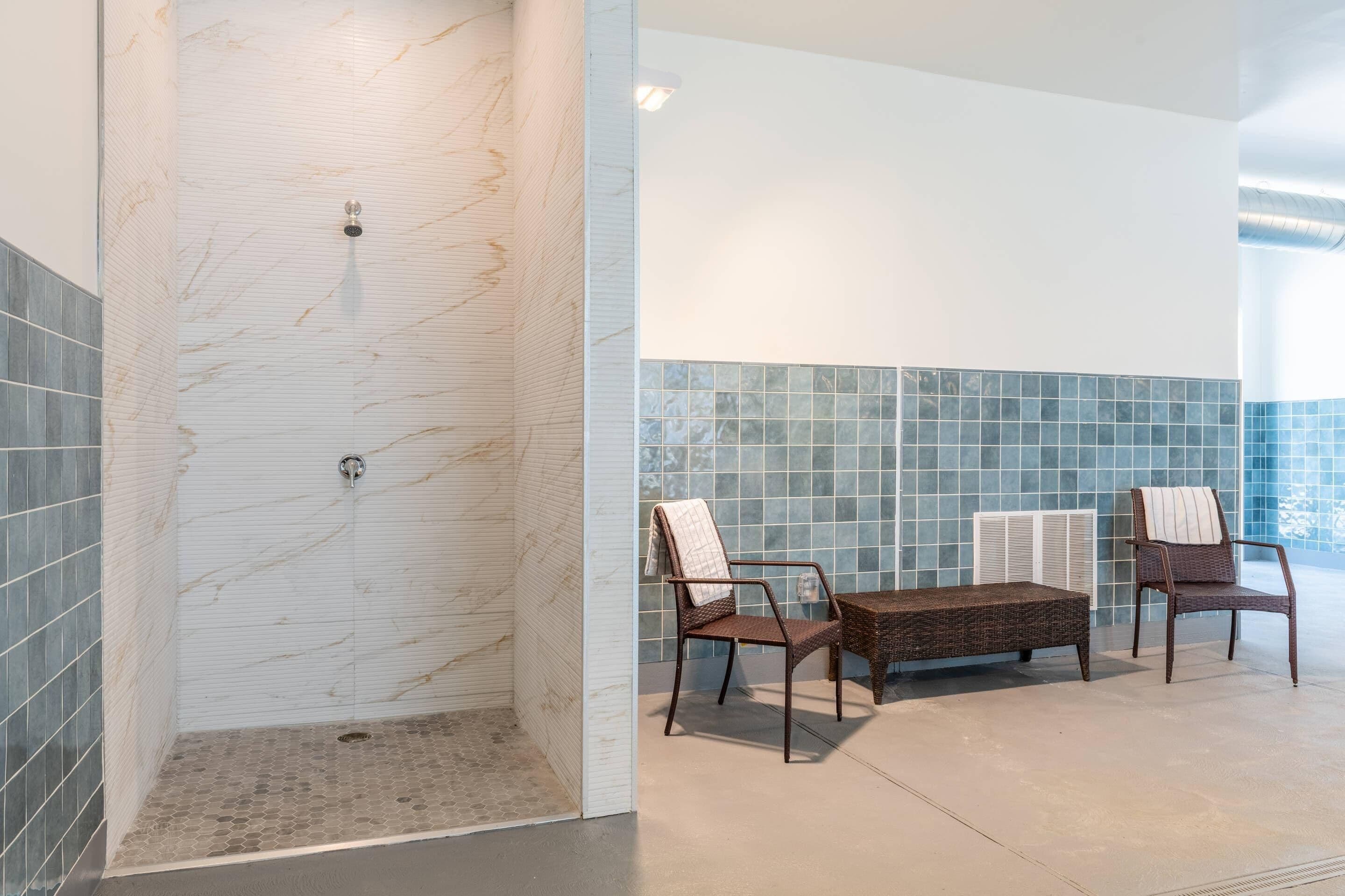 A bathroom with a shower, two wicker chairs, and a small table.