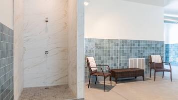 A bathroom with a shower, two wicker chairs, and a small table.