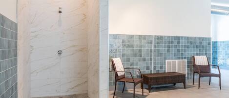 A bathroom with a shower, two wicker chairs, and a small table.
