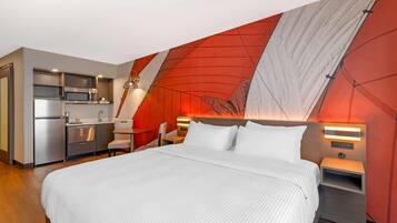 A modern hotel room with a large bed, a kitchenette, and a unique red and white wall design.
