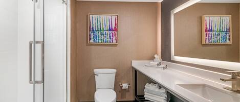 A modern bathroom with a glass shower enclosure, a white toilet, a large mirror, and a white sink with a towel rack.