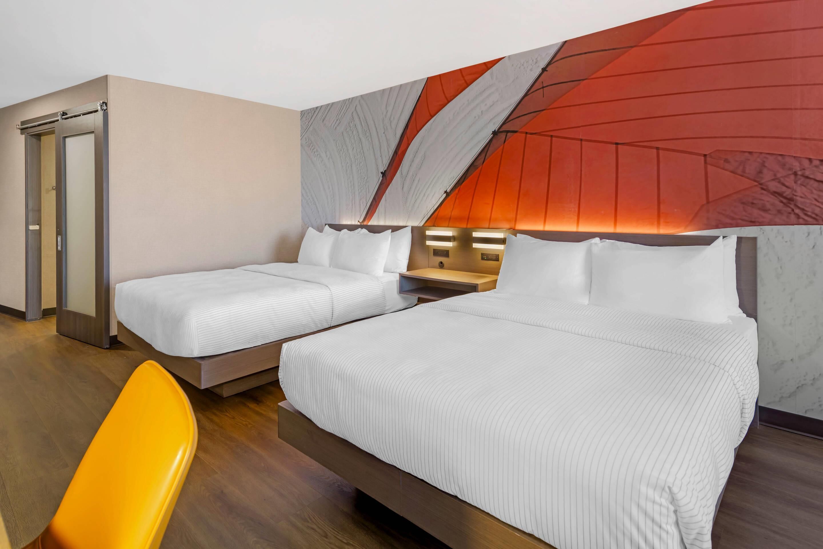 A hotel room with two beds, a wooden floor, a door, and a red accent wall.