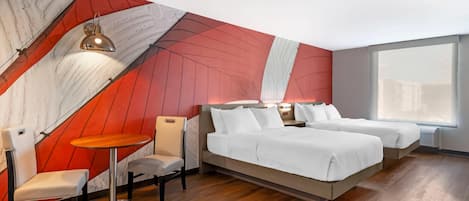 Una habitación de hotel moderna con una cama grande, dos mesitas de noche, una mesa redonda pequeña y una silla. La habitación presenta un diseño de pared único en rojo y blanco y ventanas amplias.