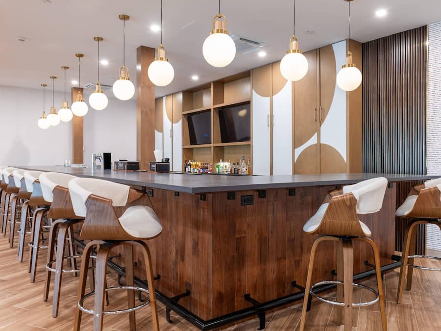 A modern bar area with a wooden bar counter, multiple stools, and pendant lighting.