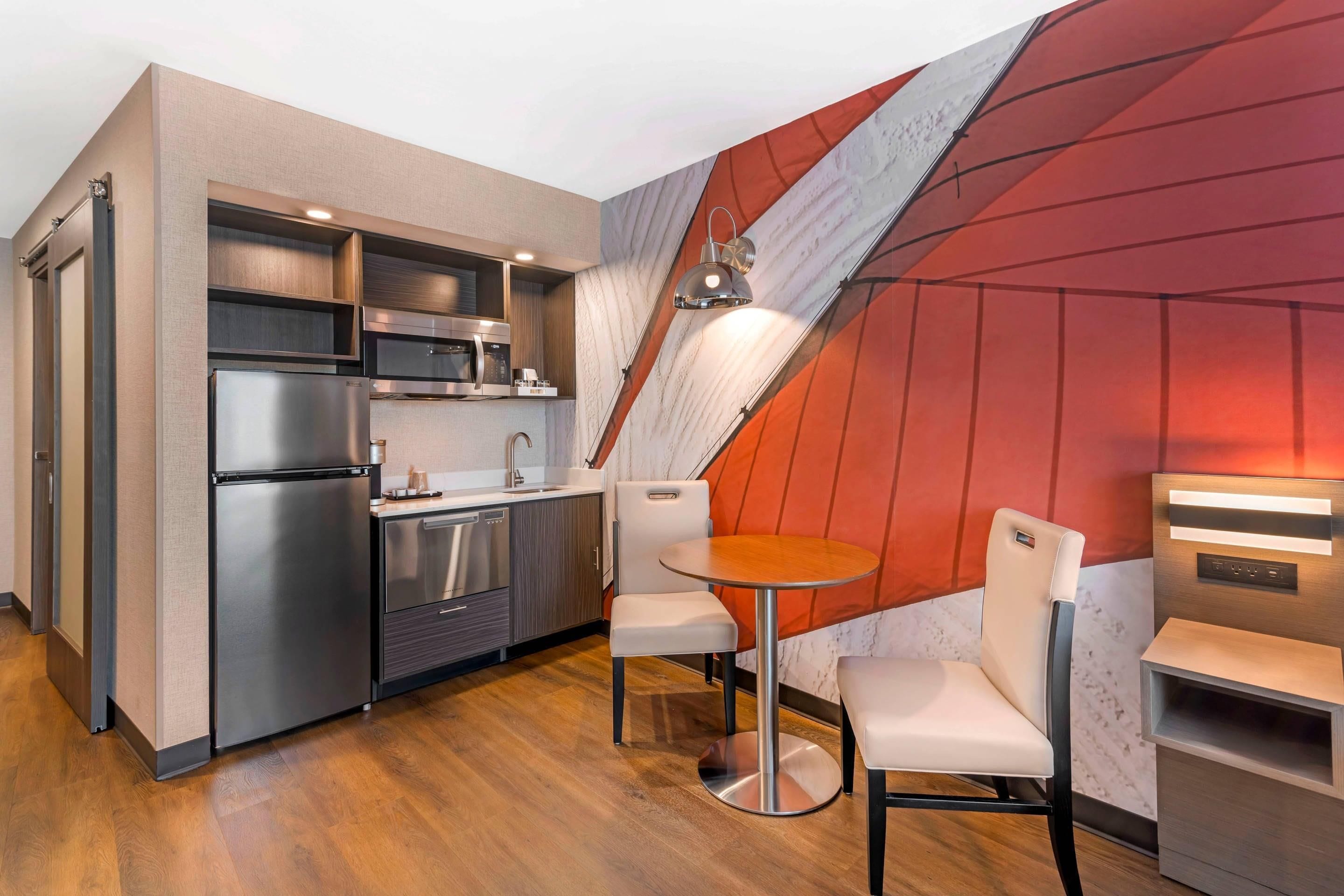 Eine moderne Küche mit Edelstahlgeräten, ein Essbereich mit rundem Tisch und Stühlen sowie ein auffälliges Wanddesign in Rot und Weiß.