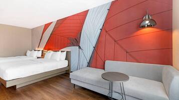 A hotel room with a bed, a sofa, a small table, and a wall with geometric patterns.