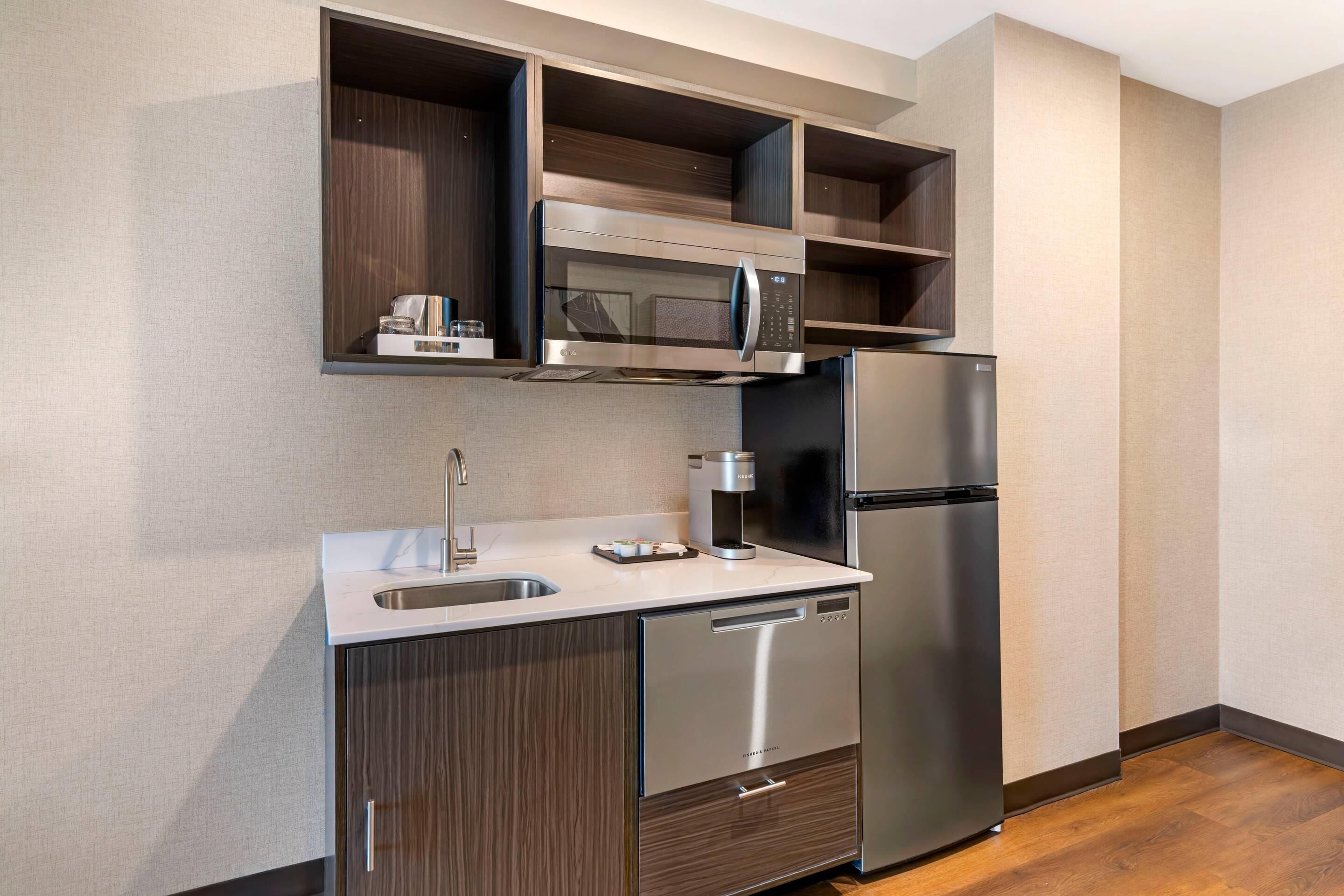 A modern kitchen with a stainless steel refrigerator, microwave, and dishwasher, wooden cabinets, and a built-in sink.
