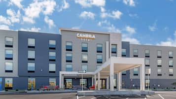 A modern hotel with a 'CAMBRIA' sign, a covered entrance, and a parking lot.