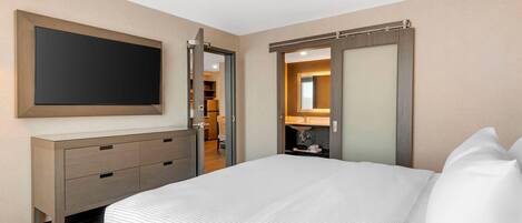 A hotel room with a bed, a TV, a dresser, and a bathroom visible through an open door.
