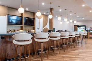 Zona de bar con varios taburetes, una barra con televisor y un mostrador de bebidas.