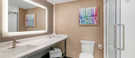 A modern bathroom with a large mirror, a white sink, a toilet, and a glass shower enclosure.