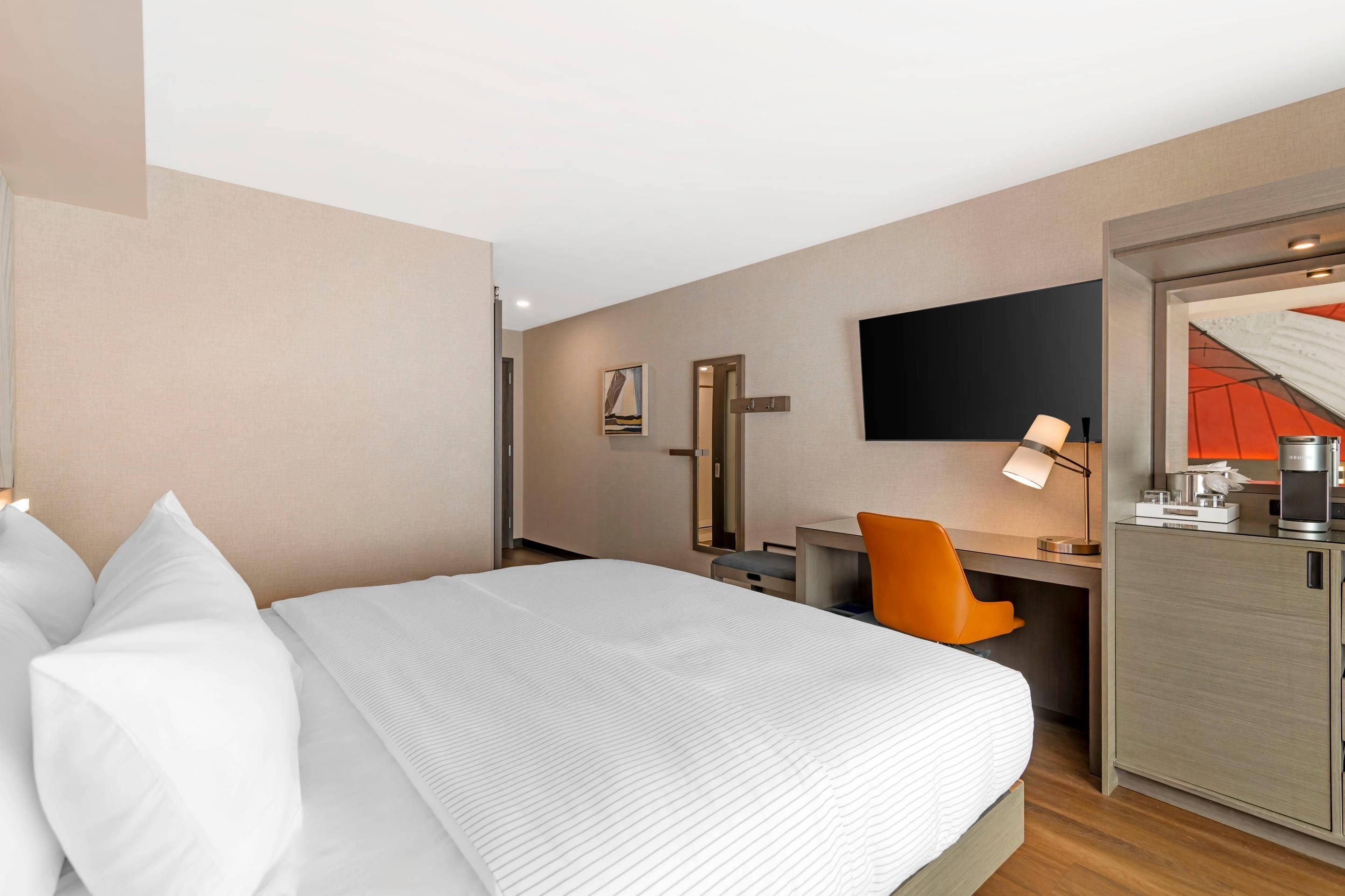 Habitación de hotel con cama, escritorio, silla, televisión y minibar.