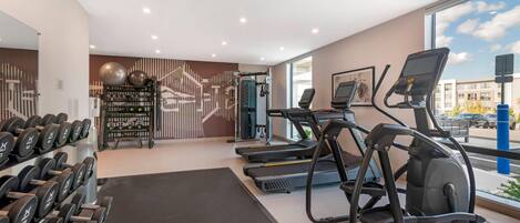 Un gimnasio con cintas de correr, mancuernas y pelotas de ejercicio.