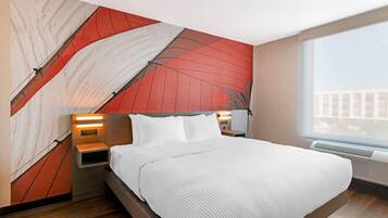 Una habitación de hotel moderna con una cama grande, una mesita de noche con una lámpara, un calentador de pared y un ventanal con vistas a la ciudad.