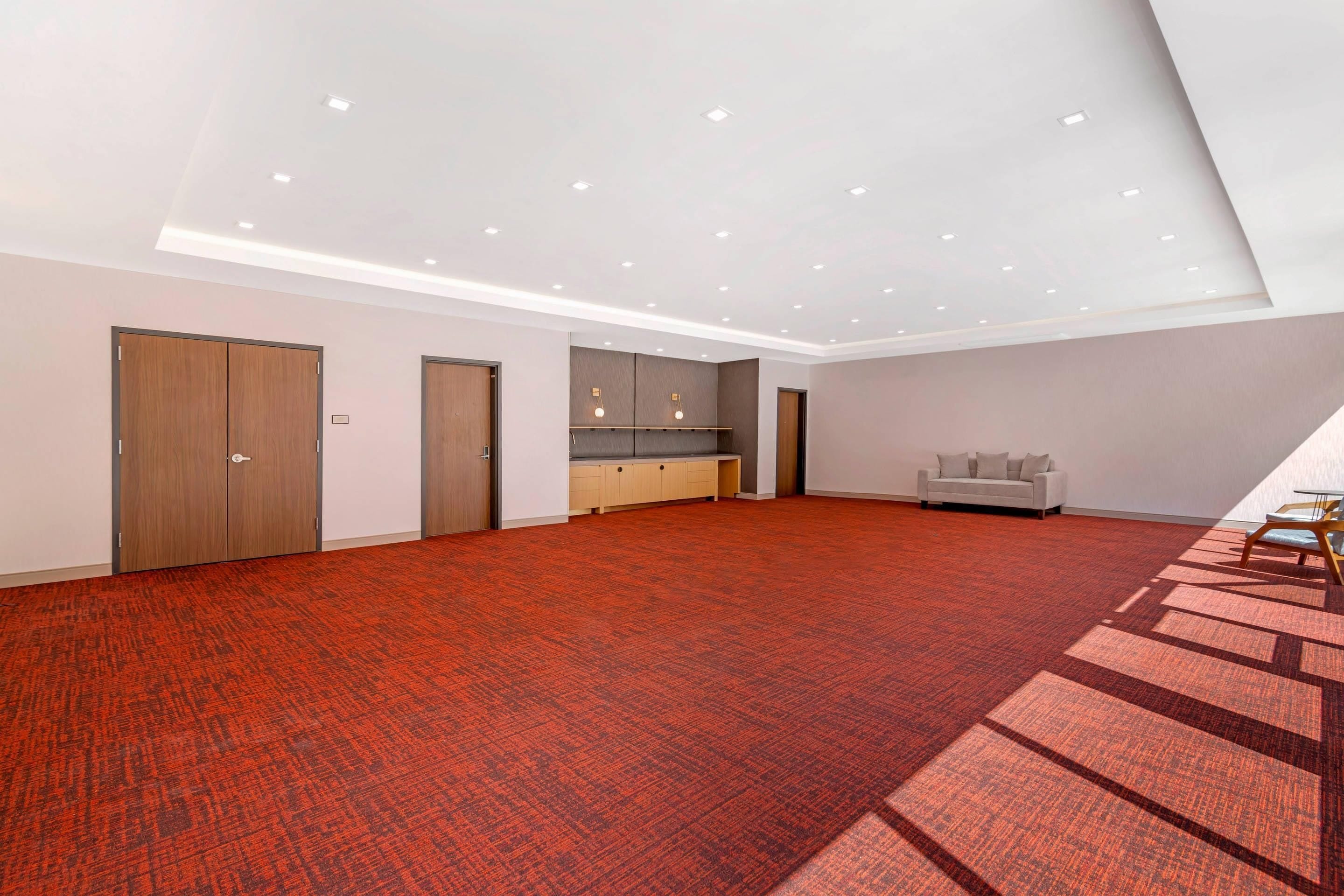 A spacious room with a red carpet, a sofa, a cabinet, and a door.