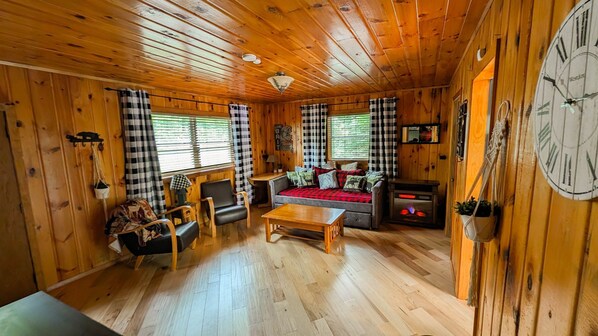 A cozy cabin interior with a sofa, chairs, a table, and a fireplace.