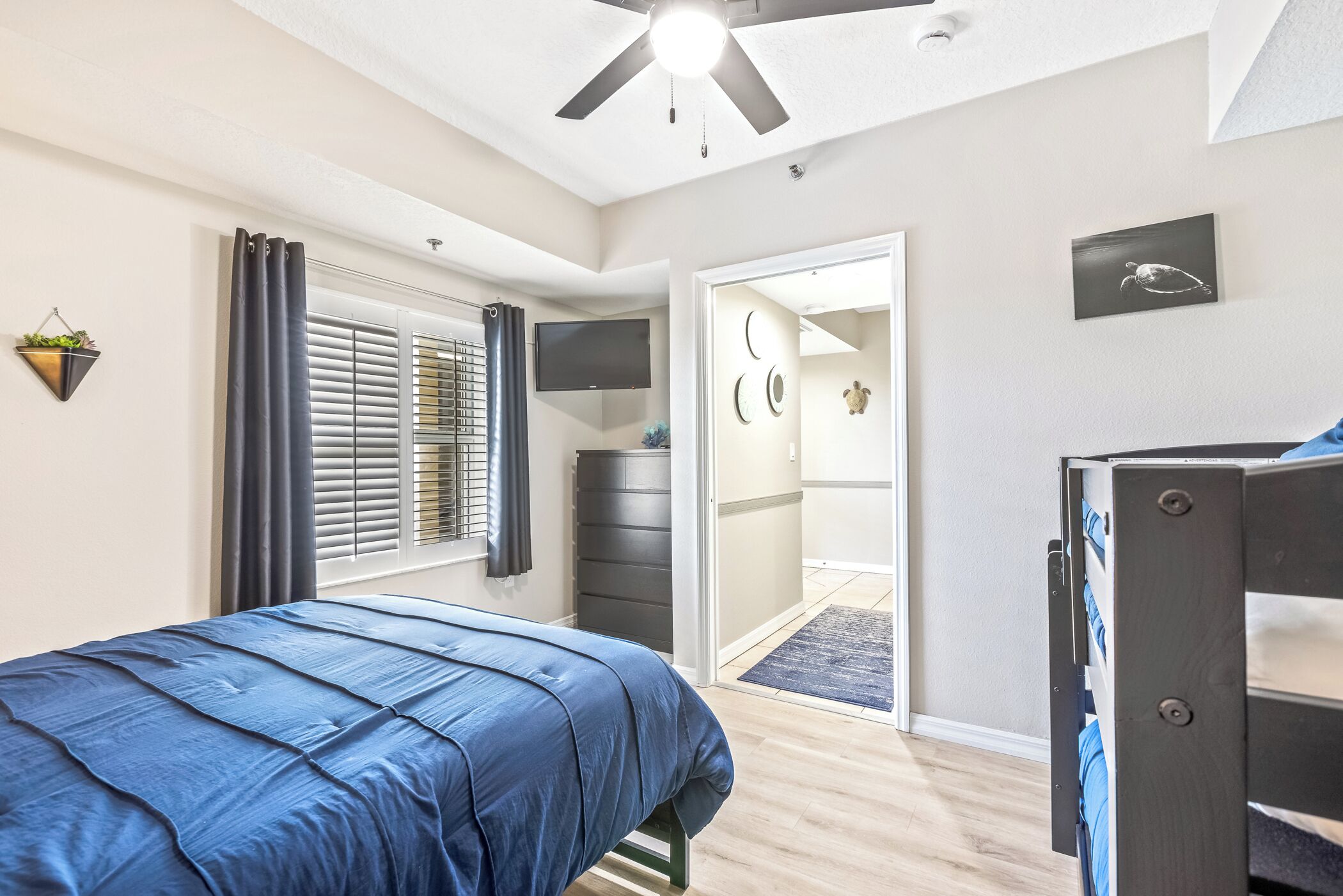Un dormitorio con cama, ventilador de techo, televisor, armario y puerta que da al baño.