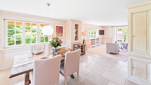 A spacious dining area with a wooden table, cushioned chairs, and a vase of flowers. - Avenarius Hüs - Reet. Kampen. Garten (Kampen (Sylt))