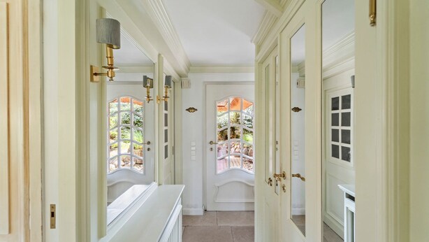 A hallway with white doors, a radiator, and a view of an outdoor patio. - Avenarius Hüs - Reet. Kampen. Garten (Kampen (Sylt))