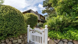 A gated entrance with a stone wall and a well-maintained hedge. - Avenarius Hüs - Reet. Kampen. Garten (Kampen (Sylt))