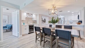 A modern kitchen with white cabinets, a wooden dining table, and a hanging light fixture. - Seagate 307—Oceanfront Condo w/ Gulf Balcony, Pool Access & Walkable Dining in Indian Shores (Indian Shores)