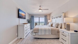 A bedroom with a bed, a nightstand, a dresser, a ceiling fan, a window with curtains, and a wall-mounted TV. - Seagate 307—Oceanfront Condo w/ Gulf Balcony, Pool Access & Walkable Dining in Indian Shores (Indian Shores)