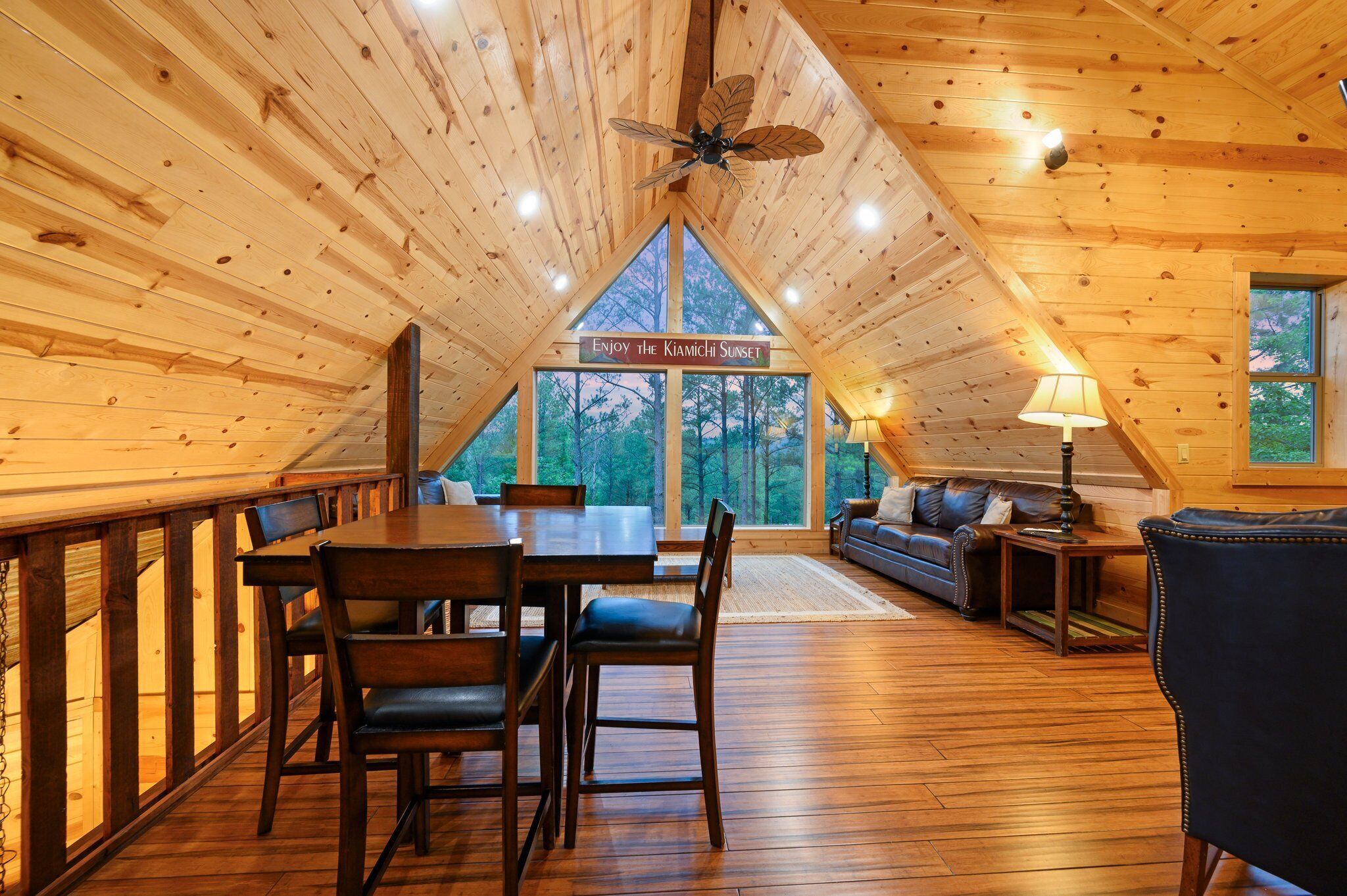 Un interior de madera con una mesa de comedor, sillas y un sofá. Hay un letrero que dice "Enjoy the Kiamichi Sunset".