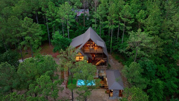 Eine Hütte, umgeben von dichtem Wald, mit einer sichtbaren Terrasse und einem Schwimmbad.
